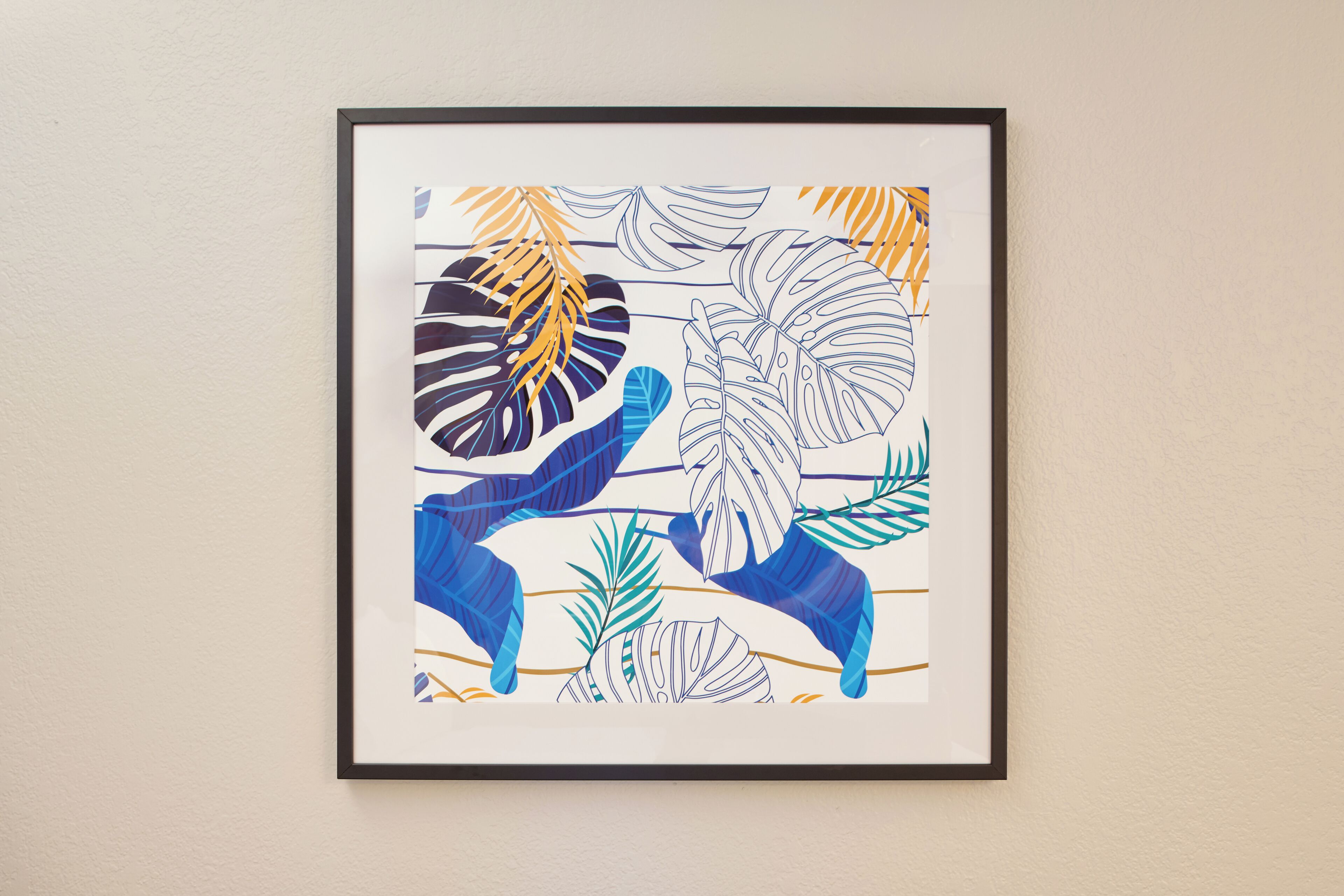 A framed artwork with tropical leaf patterns.