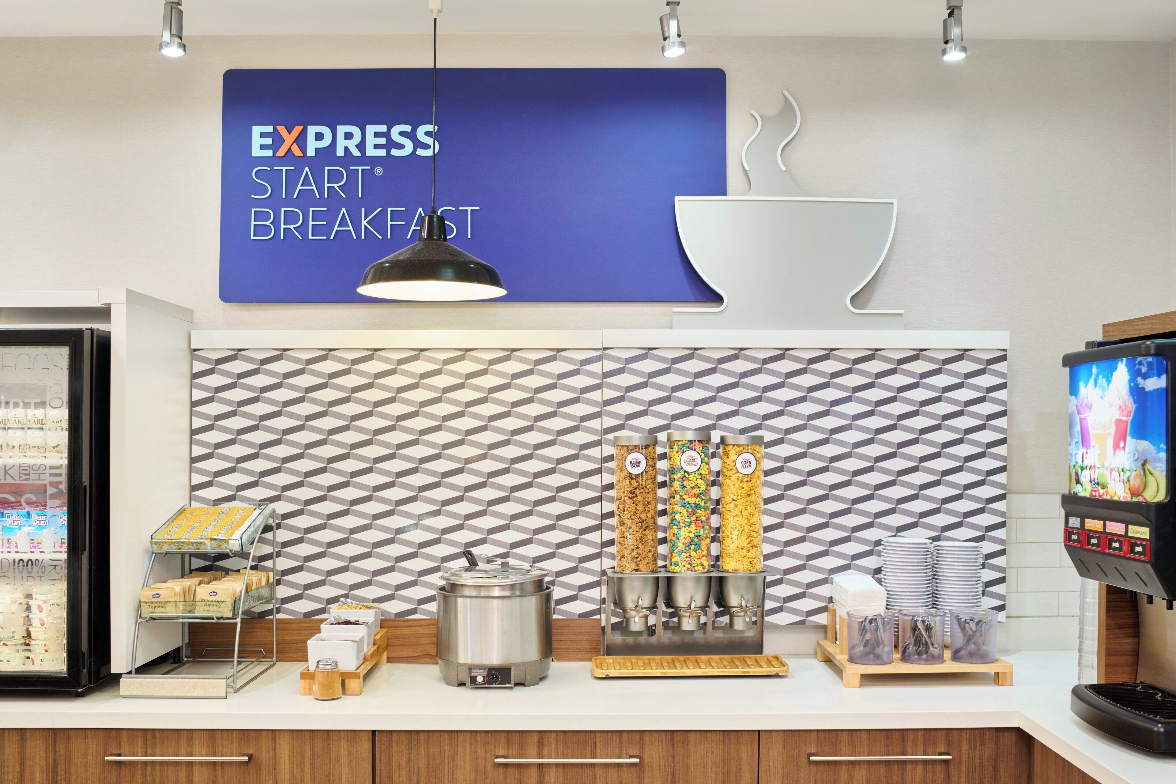 A breakfast area with a sign reading "EXPRESS START BREAKFAST," a coffee machine, a food dispenser, and a refrigerator with beverages.