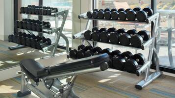 Un gimnasio con mancuernas en estanterías y una banca.