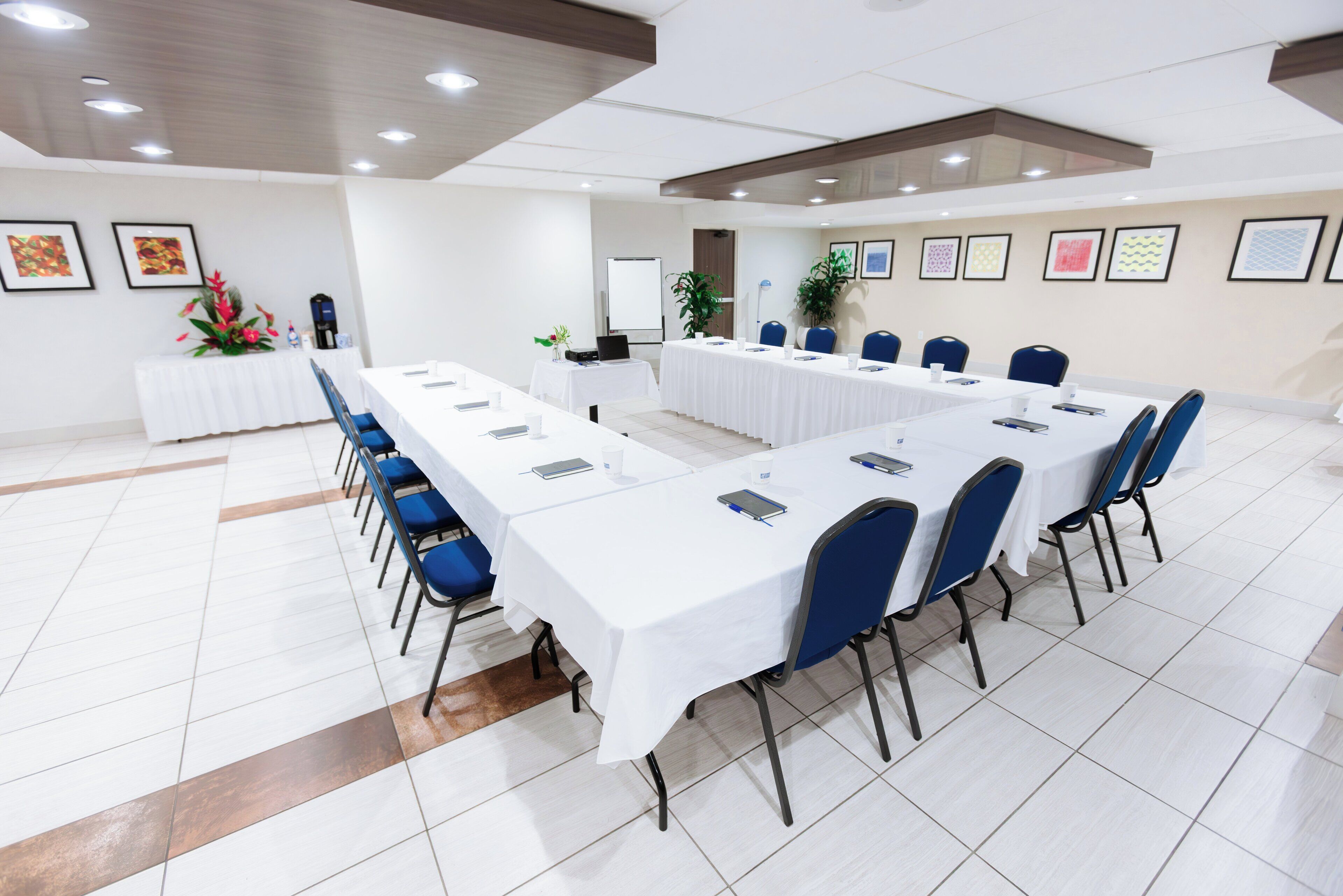A conference room with a long table, blue chairs, and white tablecloths.