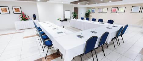 Ein Konferenzraum mit einem langen Tisch, blauen Stühlen und weißen Tischdecken.