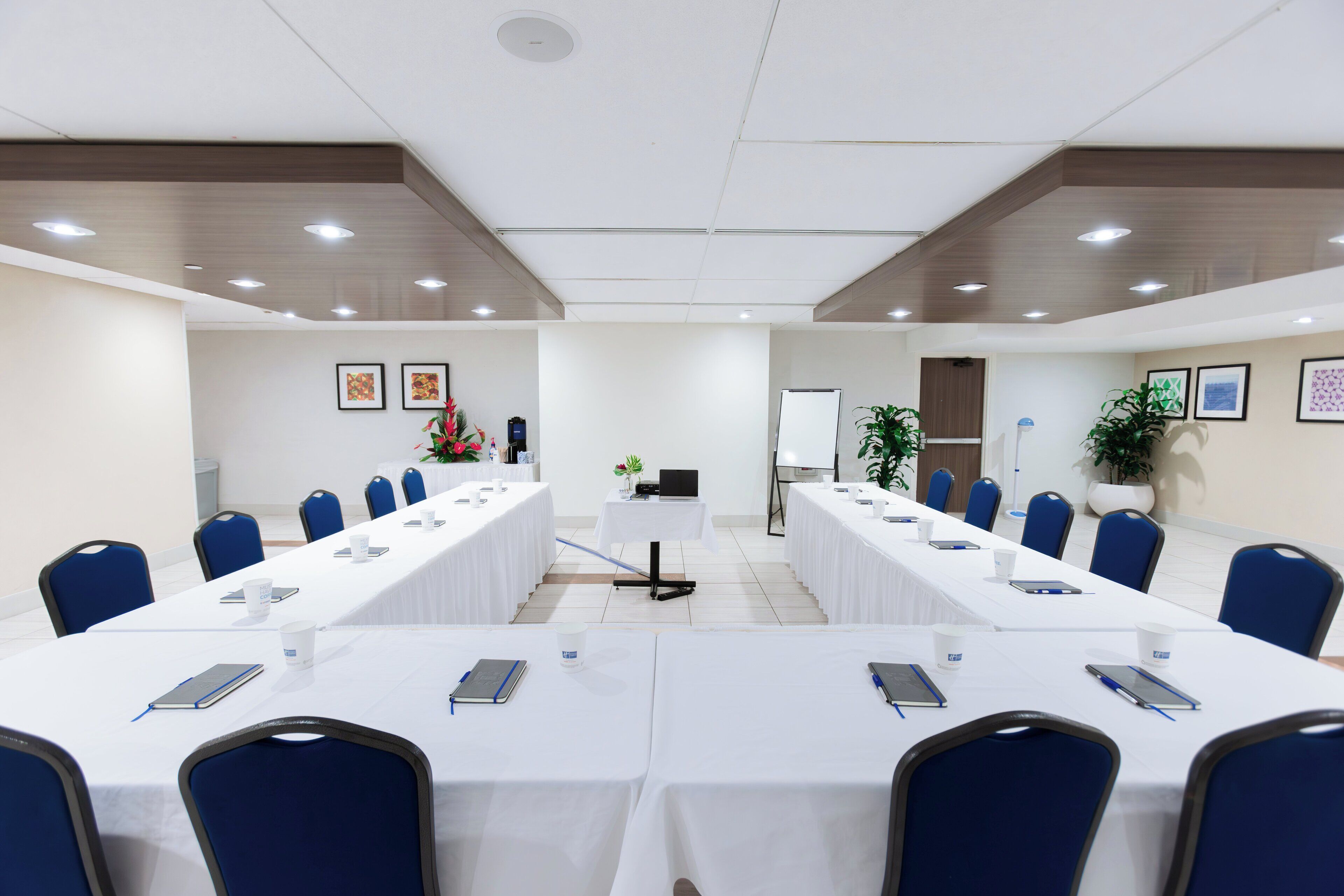 Un salón de conferencias con largas mesas, sillas azules y manteles blancos.