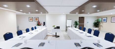 Un salón de conferencias con largas mesas, sillas azules y manteles blancos.