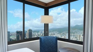 A hotel room with a large window offering a city view, a blue upholstered chair, a small round table, and a floor lamp.