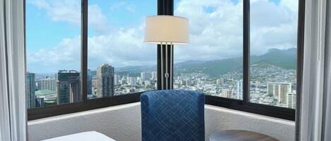 Habitación de hotel con un ventanal amplio que ofrece vistas de la ciudad, un sillón tapizado en azul, una mesita redonda y una lámpara de pie.