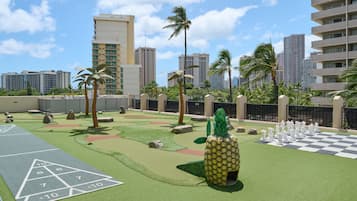 A rooftop garden with a checkered game table, a pineapple sculpture, and palm trees.