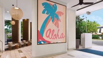 A modern lobby with wicker furniture, a large 'Aloha' sign, and a ceiling fan.
