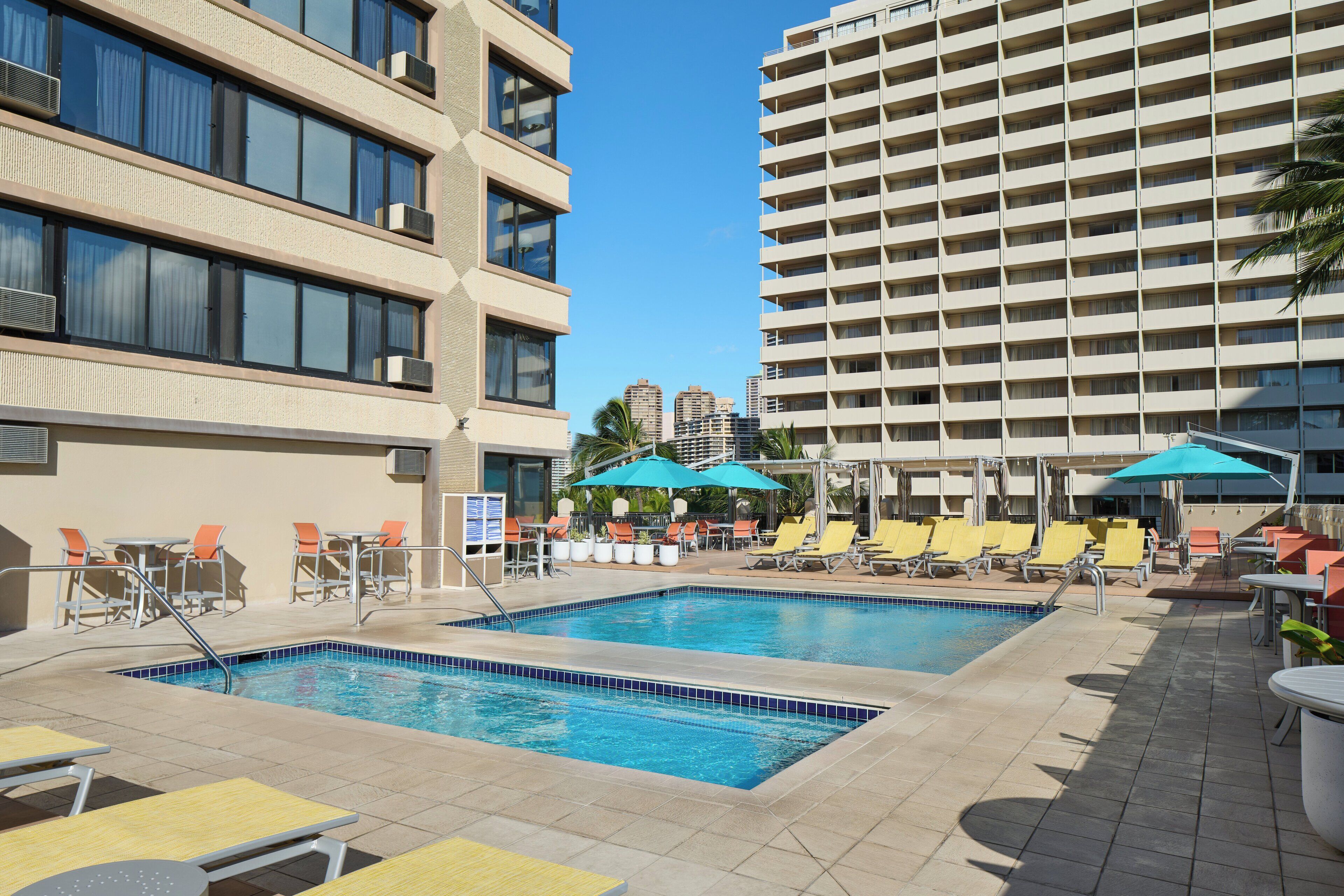 A rooftop pool area with multiple pools, lounge chairs, and umbrellas.