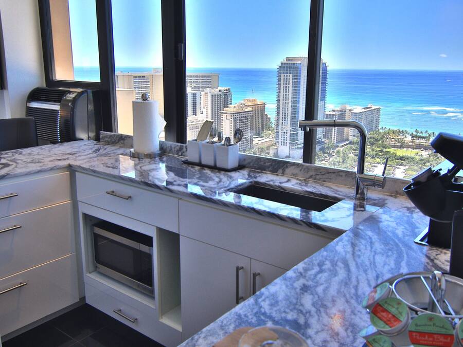 A kitchen with a view of the ocean and cityscape, featuring a marble countertop, modern appliances, and a built-in oven.