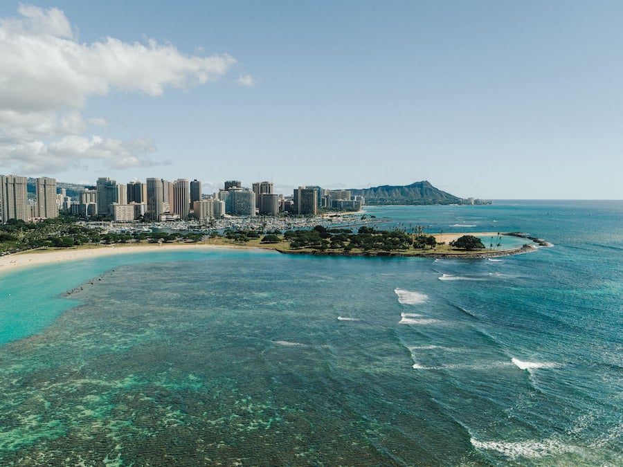 A coastal cityscape with a beach, clear blue waters, and a mountain in the background.