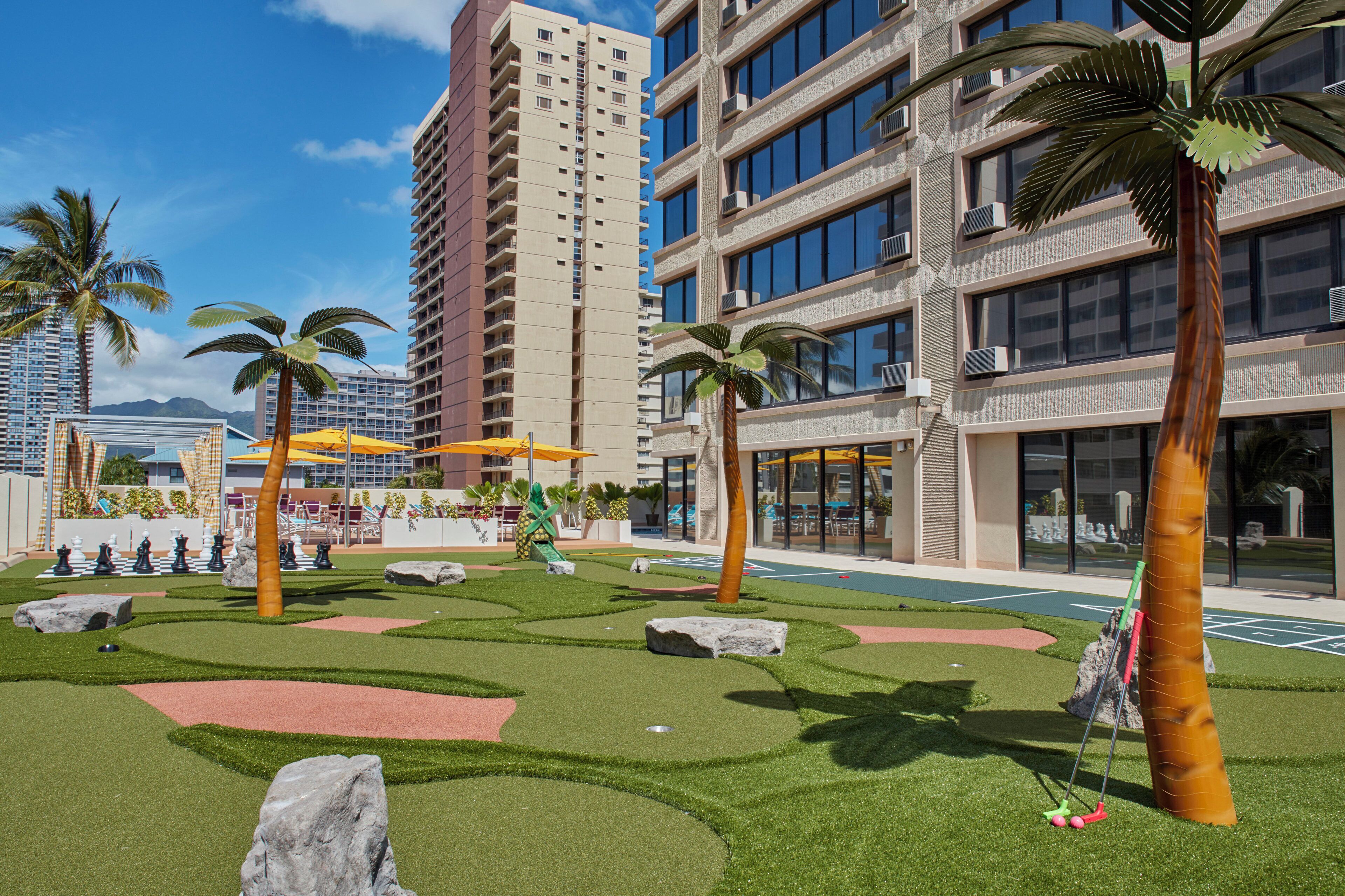 A landscaped outdoor area with artificial grass, palm trees, and a chessboard.