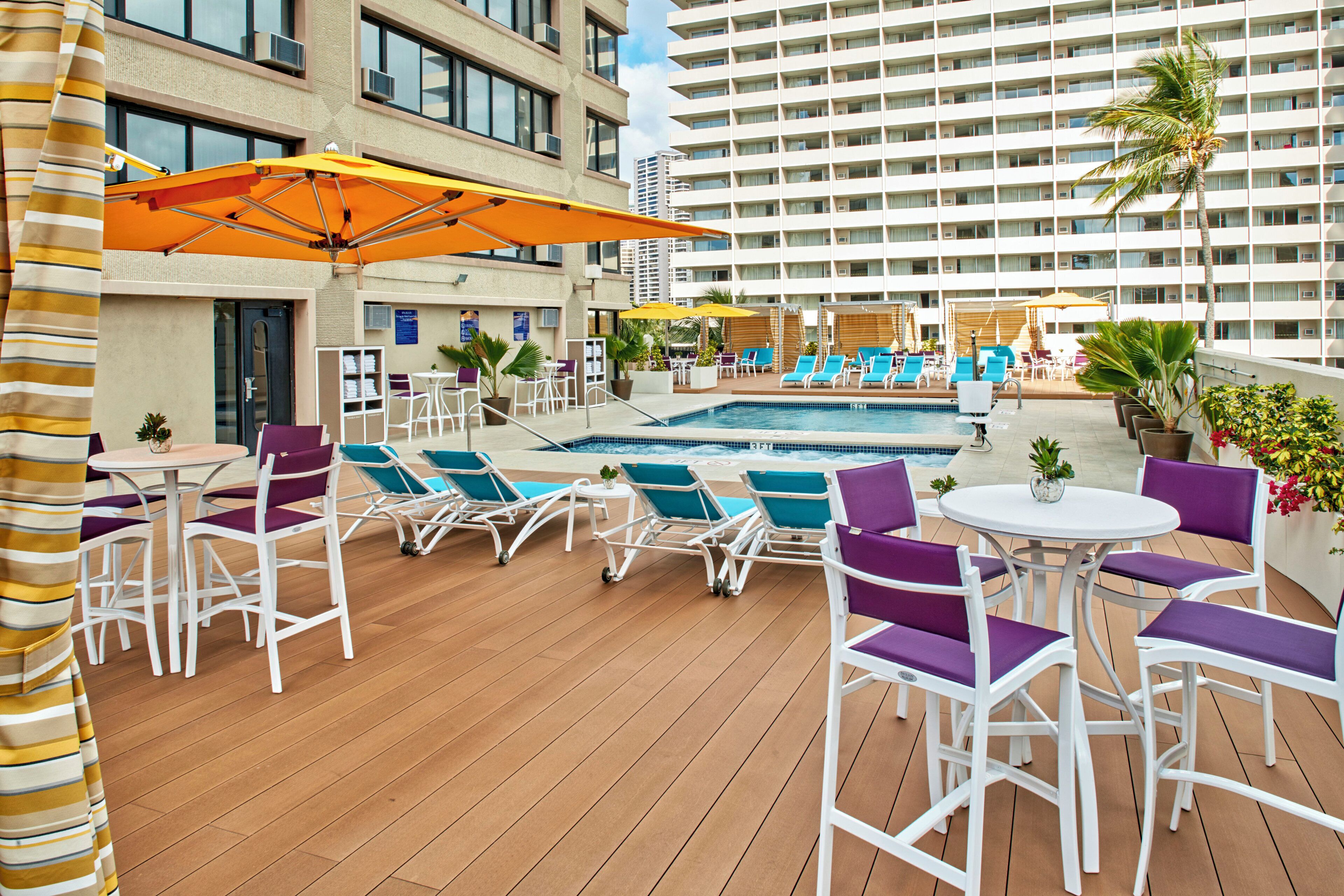 Un espace piscine aménagé sur le toit, avec des chaises longues et des parasols, entouré d’un immeuble de grande hauteur.