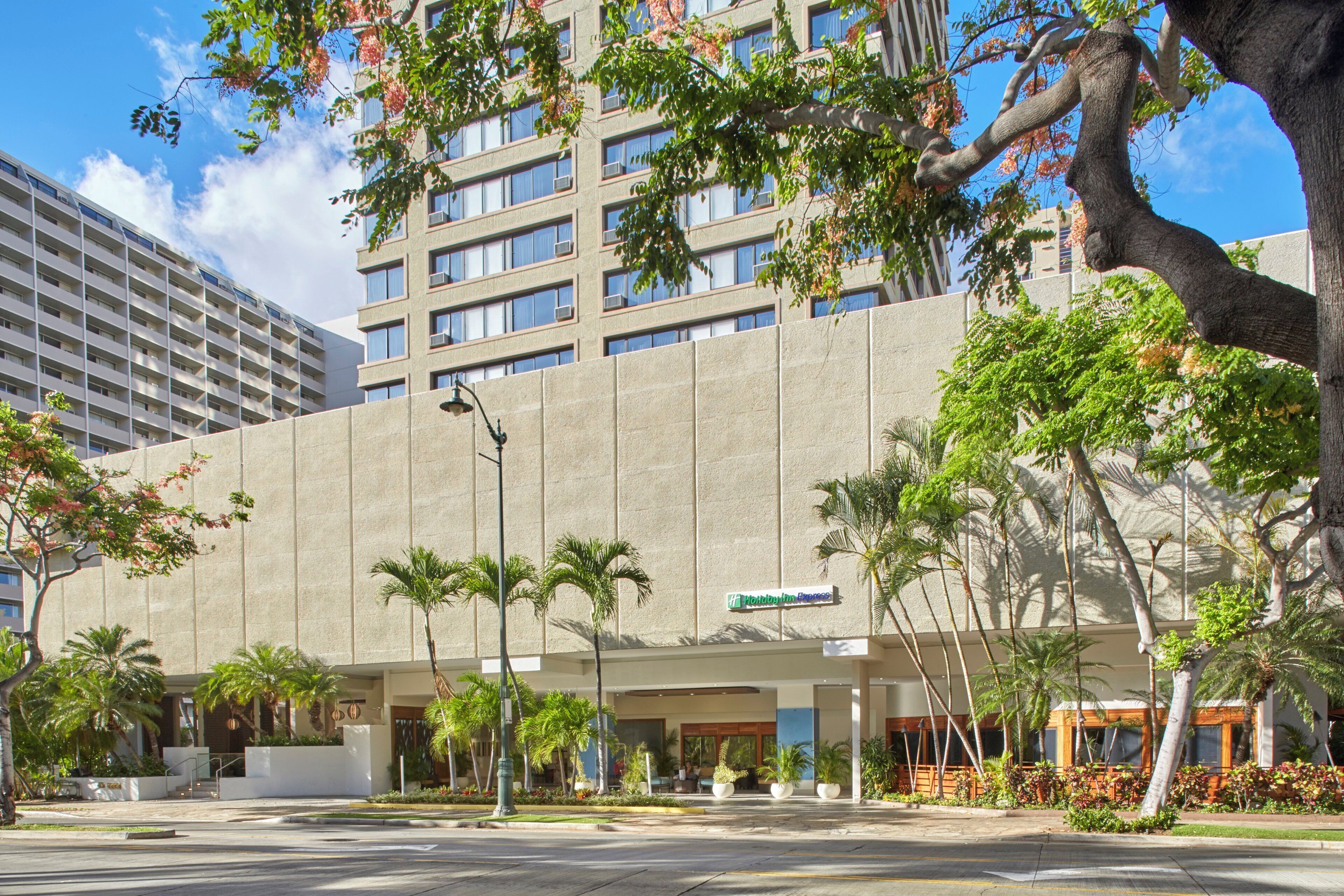 A modern hotel with a flat facade, palm trees, and a clear sky.