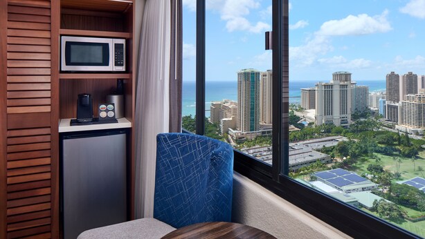A compact room with a view of a cityscape and the ocean. It includes a microwave, a coffee machine, and a seating area with a view. - Holiday Inn Express Waikiki by IHG (Honolulu)