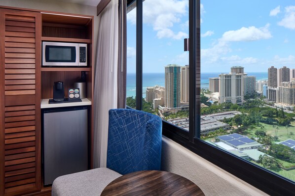 A compact room with a view of a cityscape and the ocean. It includes a microwave, a coffee machine, and a seating area with a view. - Holiday Inn Express Waikiki by IHG (Honolulu)