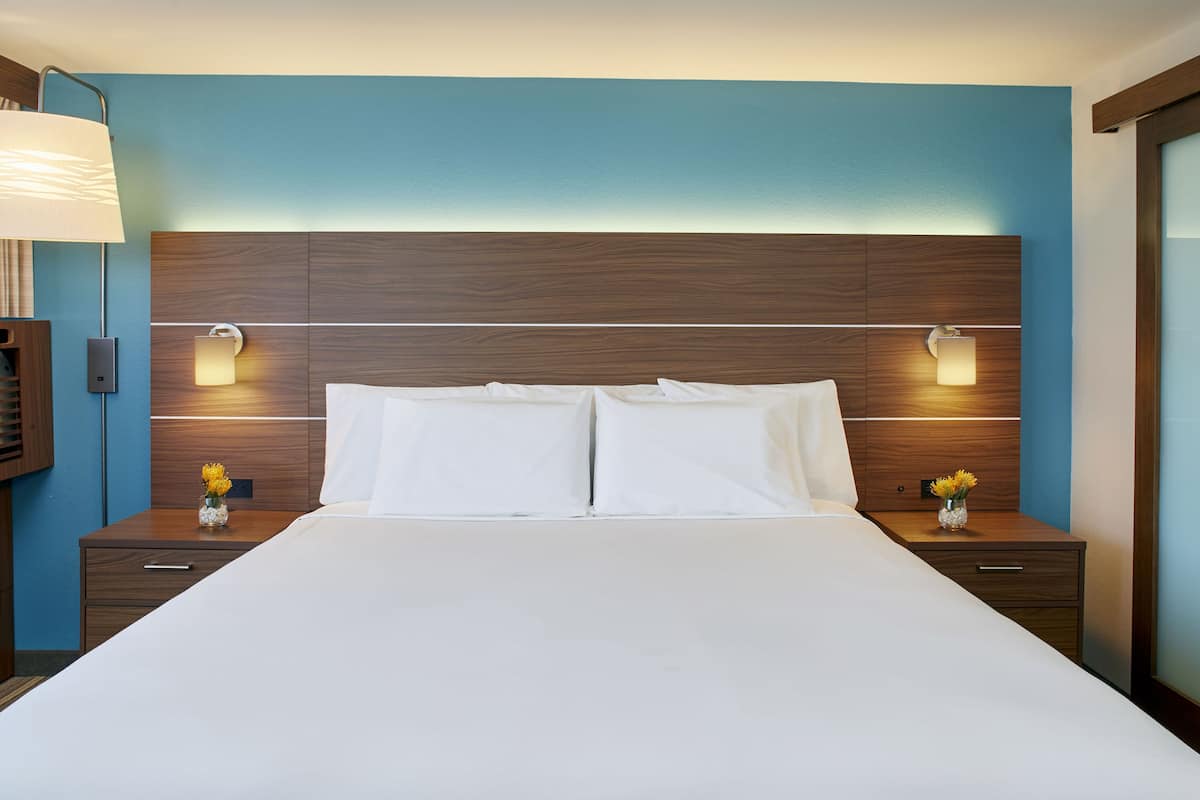 A hotel room with a large bed, wooden headboard, two bedside tables with lamps, and a vase with flowers on each table.