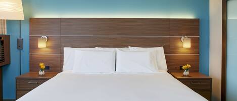 Une chambre d’hôtel avec un grand lit, une tête de lit en bois, deux tables de chevet avec des lampes et un vase de fleurs sur chaque table.