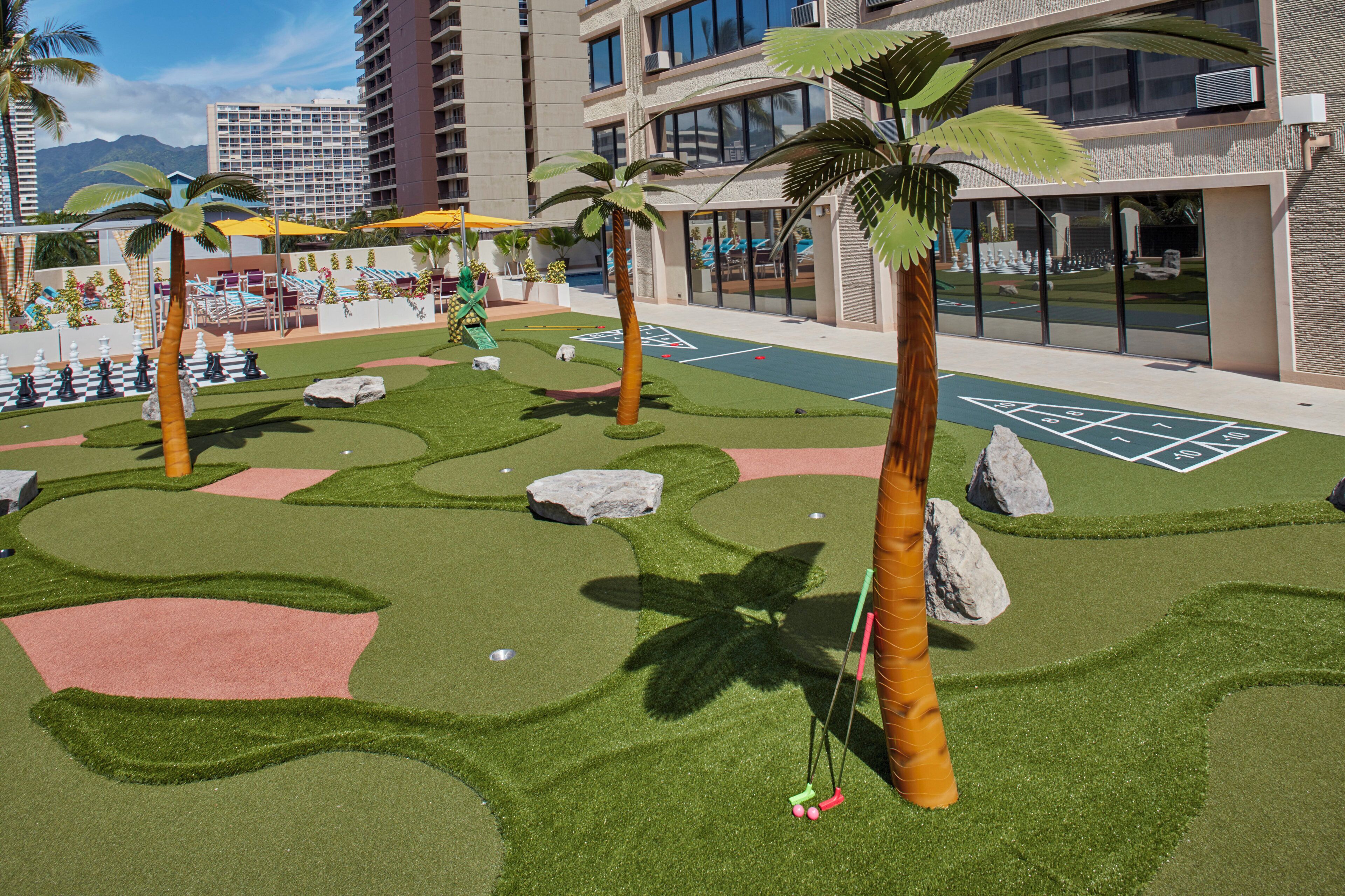 A landscaped area with artificial grass, palm trees, and a shuffleboard court.