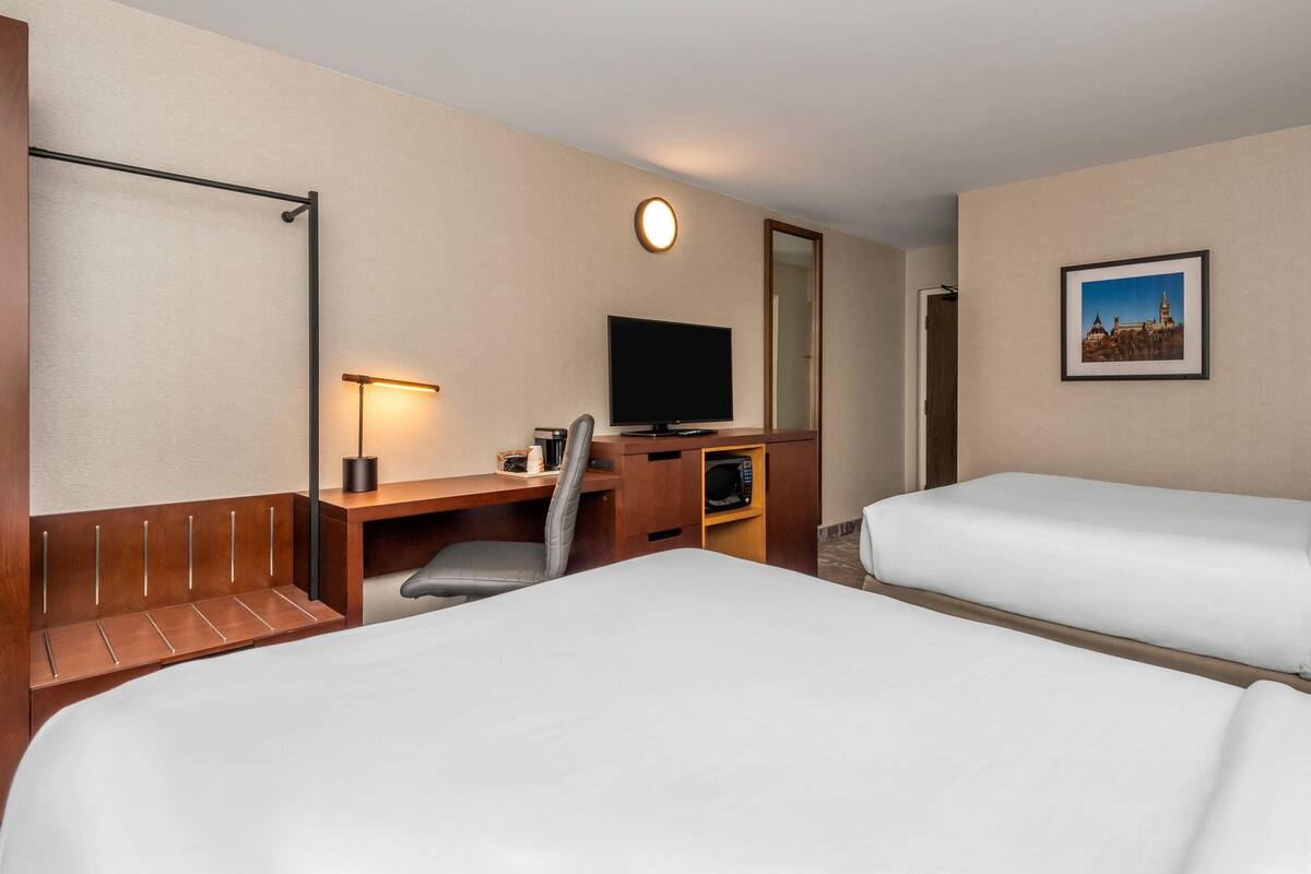 A hotel room with two beds, a desk with a chair, a television, a microwave, and a framed picture on the wall.