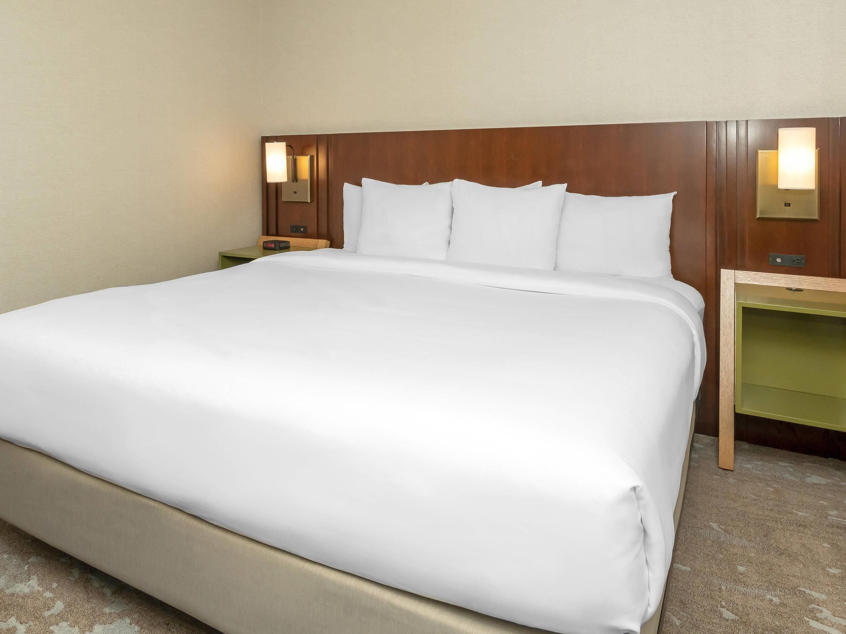 A hotel room with a large bed, two bedside tables, and wall-mounted lamps.