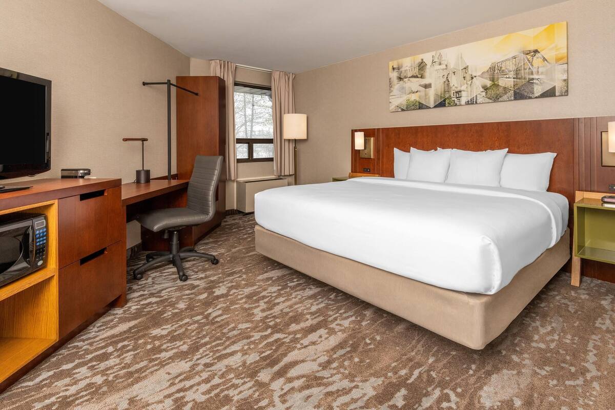 A hotel room with a bed, desk, chair, television, and artwork on the wall.