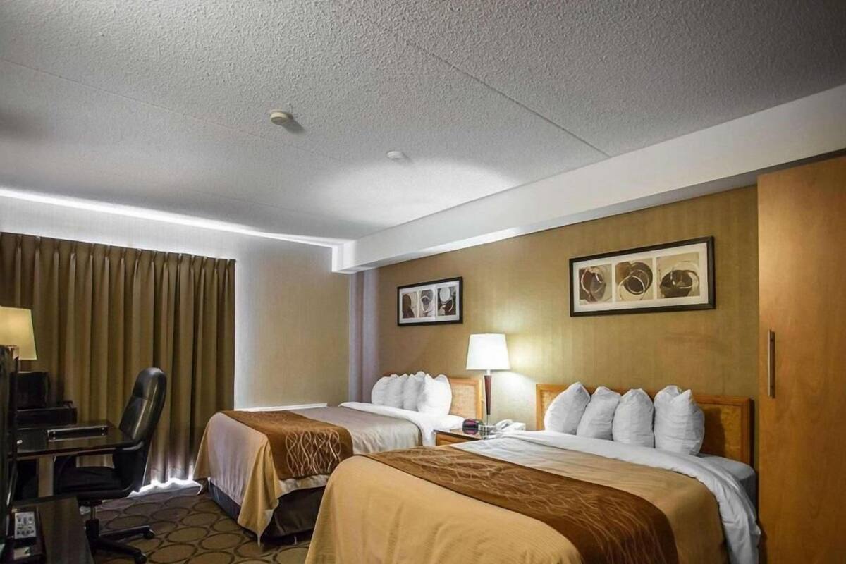 A hotel room with two beds, a desk, a chair, and a lamp.