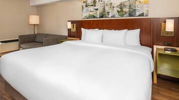 A hotel room with a large bed, a sofa, a nightstand with a lamp, and a painting on the wall.