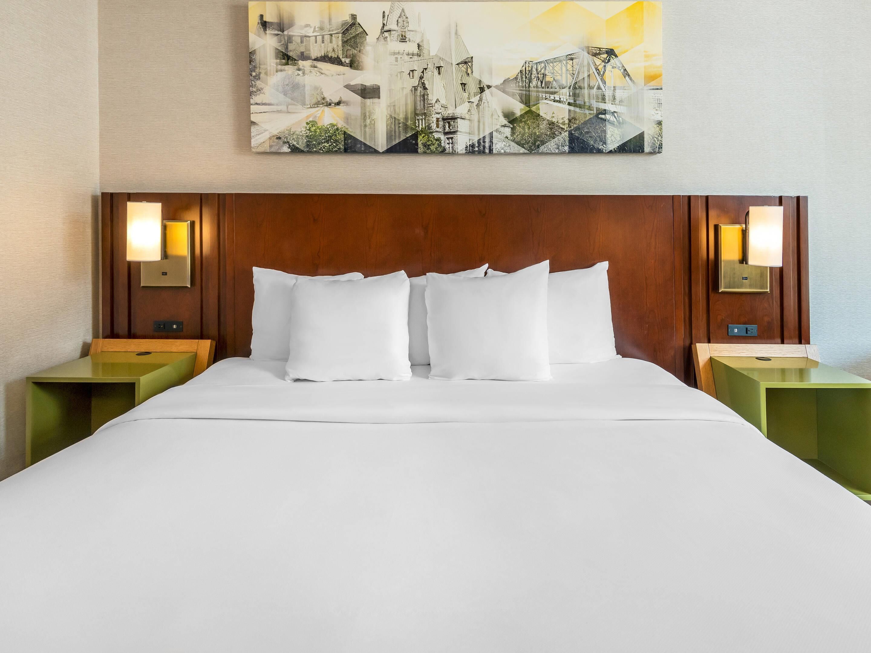 A hotel room with a wooden headboard, white bedding, and two nightstands with wall-mounted lamps.