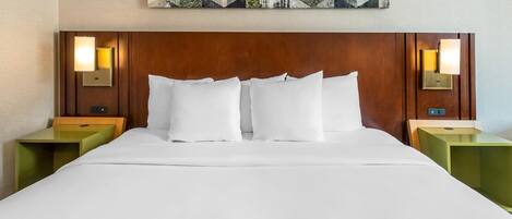 A hotel room with a wooden headboard, white bedding, and two nightstands with wall-mounted lamps.