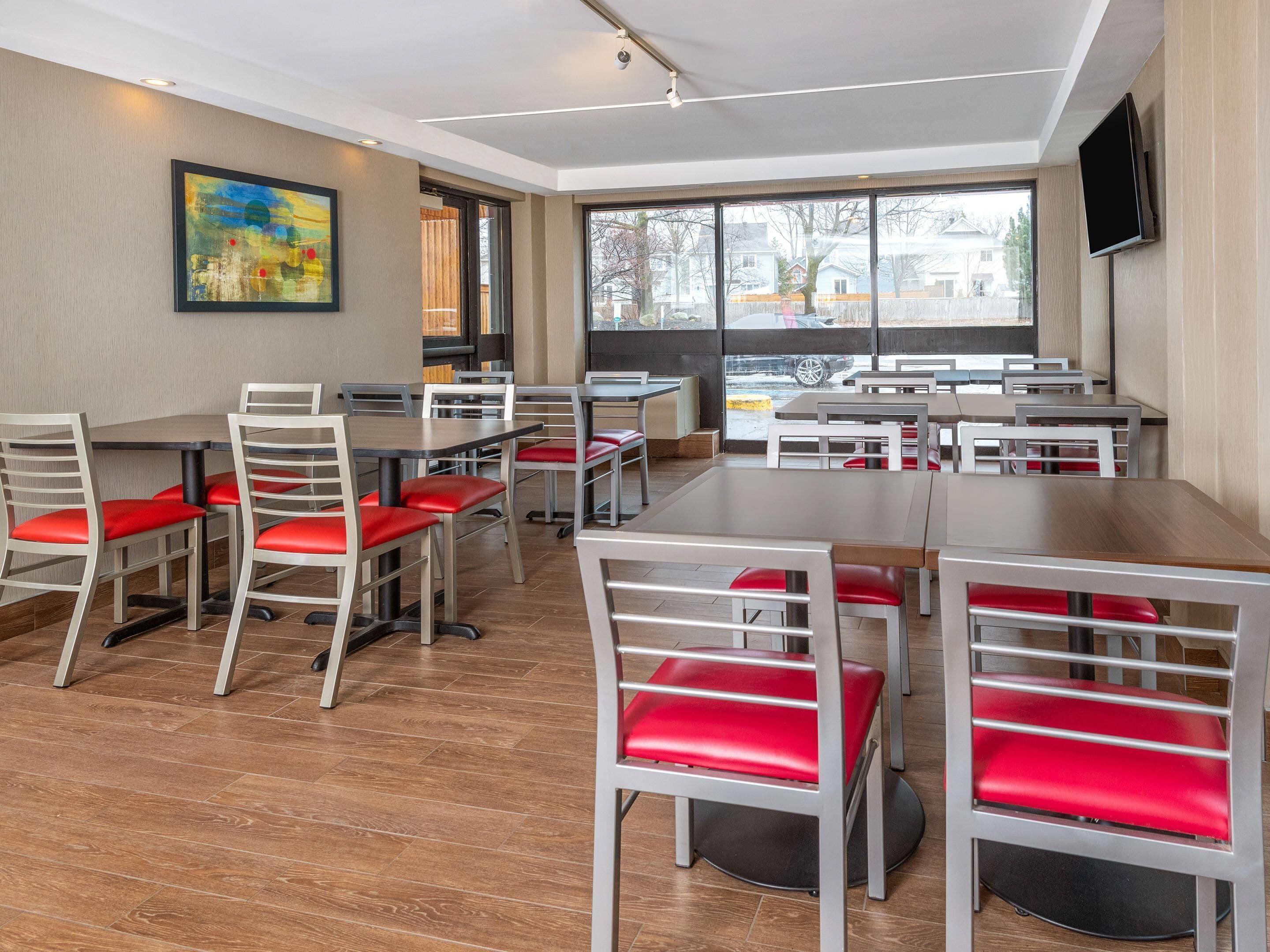 A modern dining area with tables and chairs, large windows, and a painting on the wall.