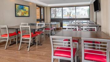 A modern dining area with tables and chairs, large windows, and a painting on the wall.