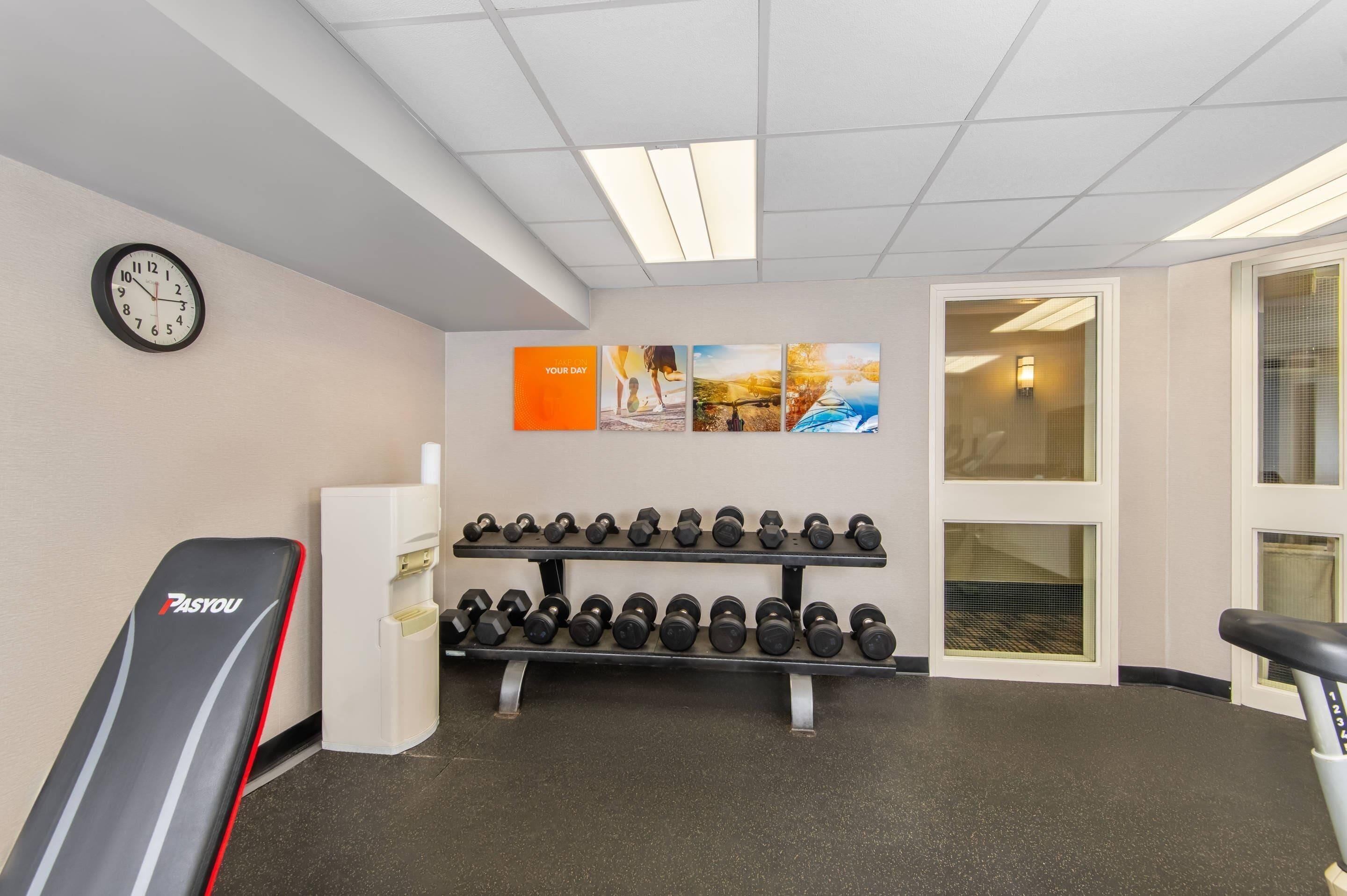 Ein Fitnessraum mit einer Uhr, Kurzhanteln und motivierenden Postern an der Wand.