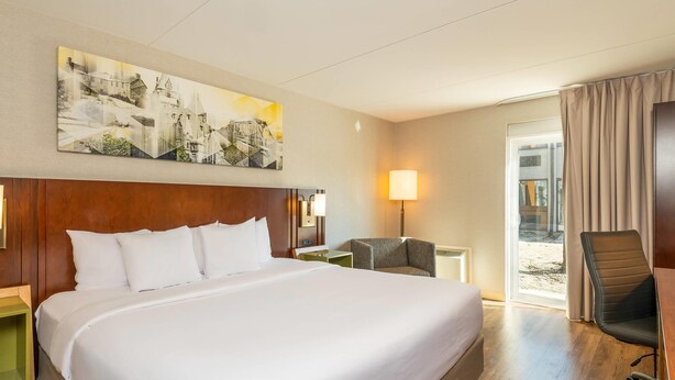 A hotel room with a large bed, a desk, a chair, a lamp, and a painting on the wall. - Comfort Inn Kanata Ottawa West (Ottawa)