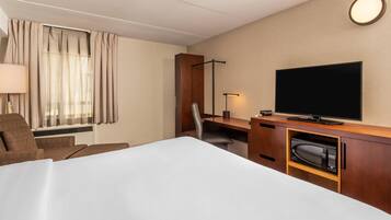 Habitación de hotel con cama, escritorio, silla, televisor, lámpara y ventana con cortinas.
