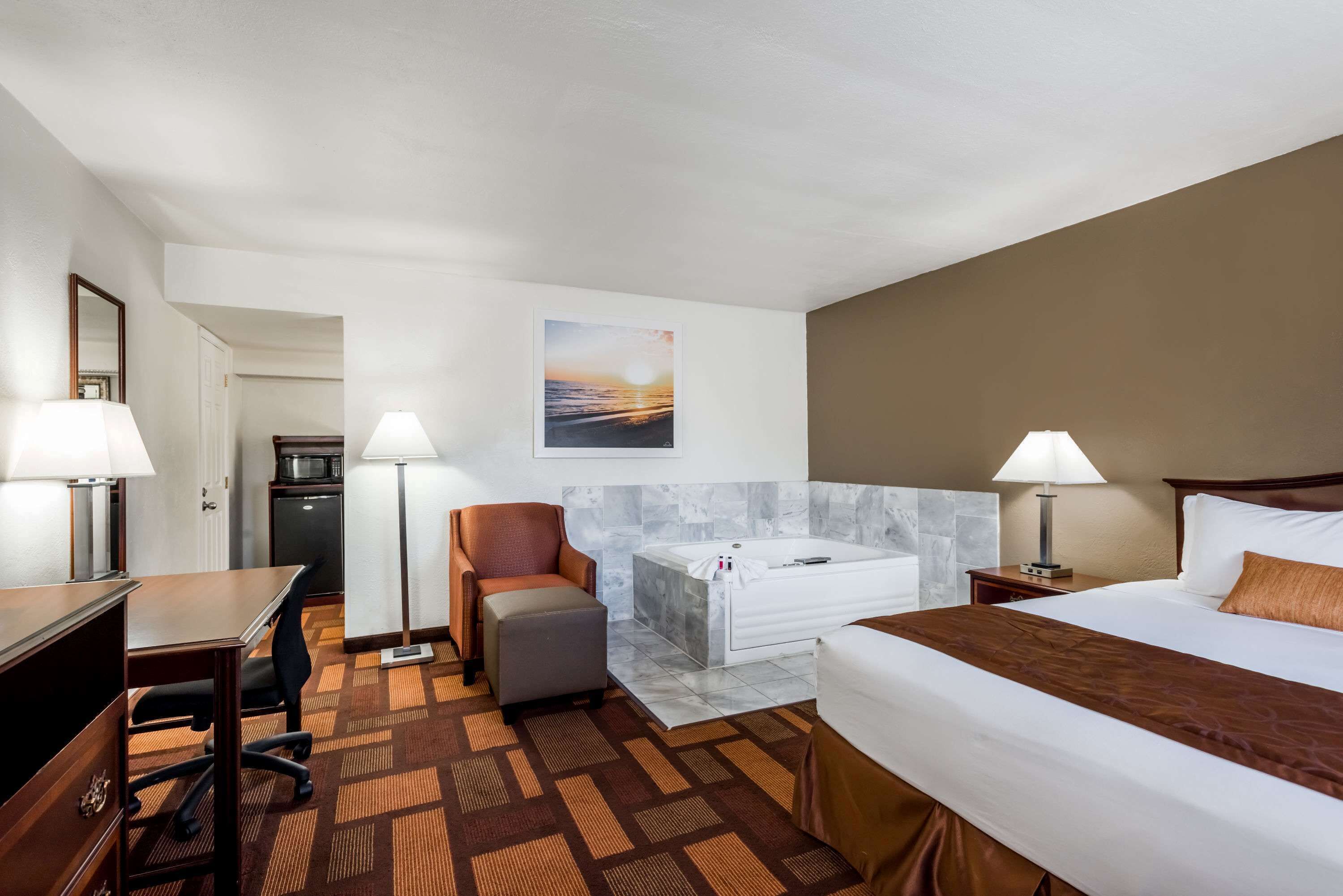 Una habitación de hotel con cama, escritorio, silla, reposapiés y una bañera grande.