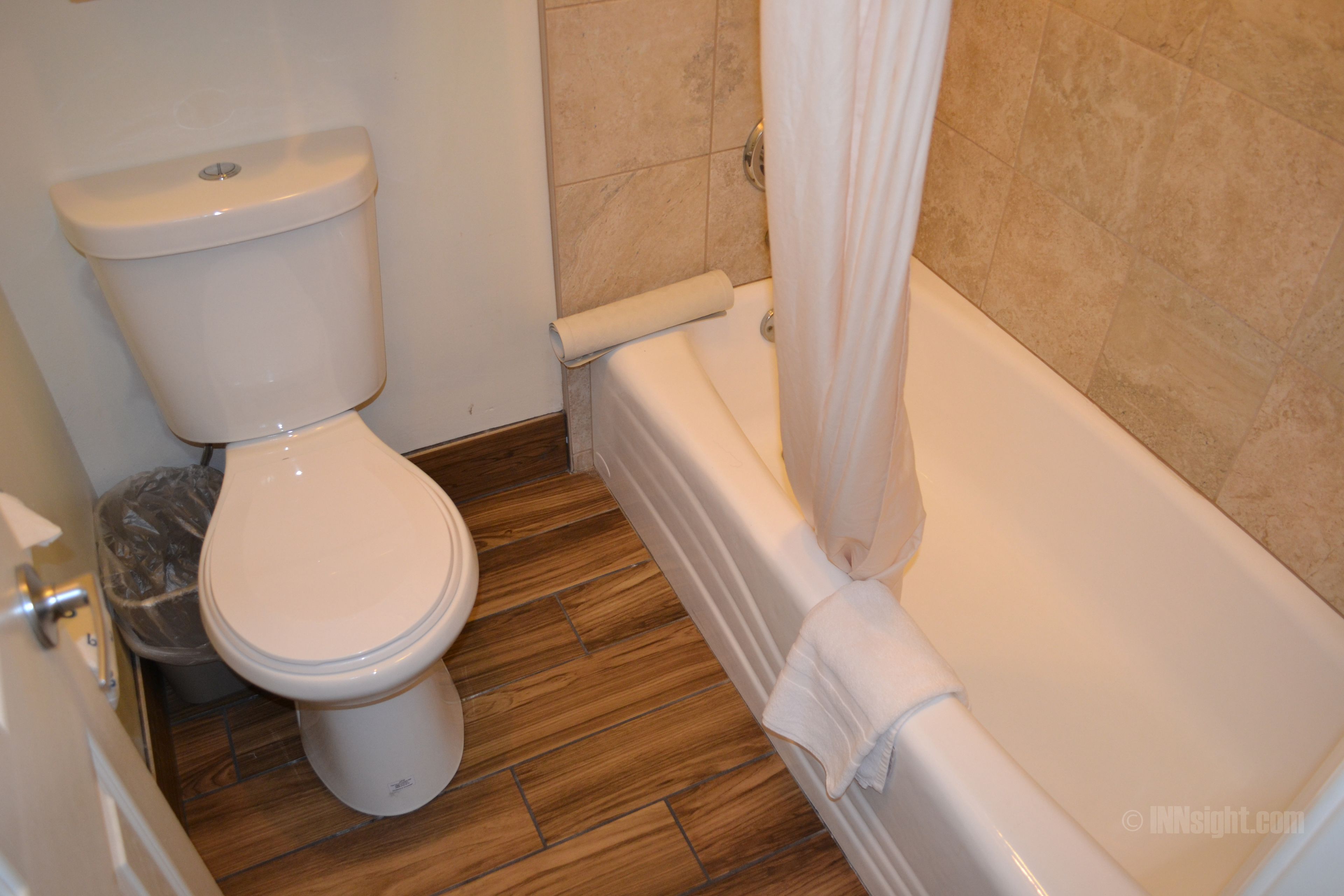 A bathroom with a toilet, a trash bin, and a bathtub.