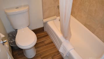 A bathroom with a toilet, a trash bin, and a bathtub.