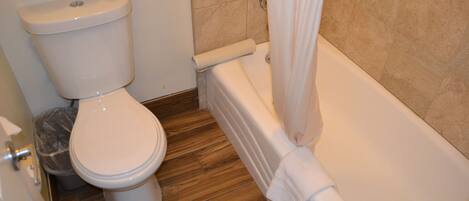 A bathroom with a toilet, a trash bin, and a bathtub.