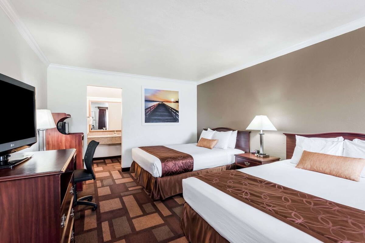 A hotel room with two beds, a desk with a TV, a chair, a desk lamp, and a painting on the wall.