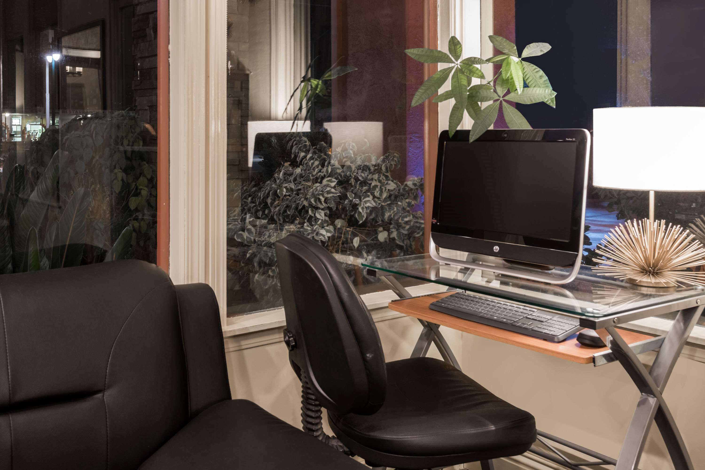A modern office space with a glass desk, a black office chair, a desktop computer, and a potted plant.