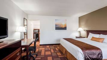 A hotel room with a bed, desk, chair, TV, lamps, and a painting on the wall.