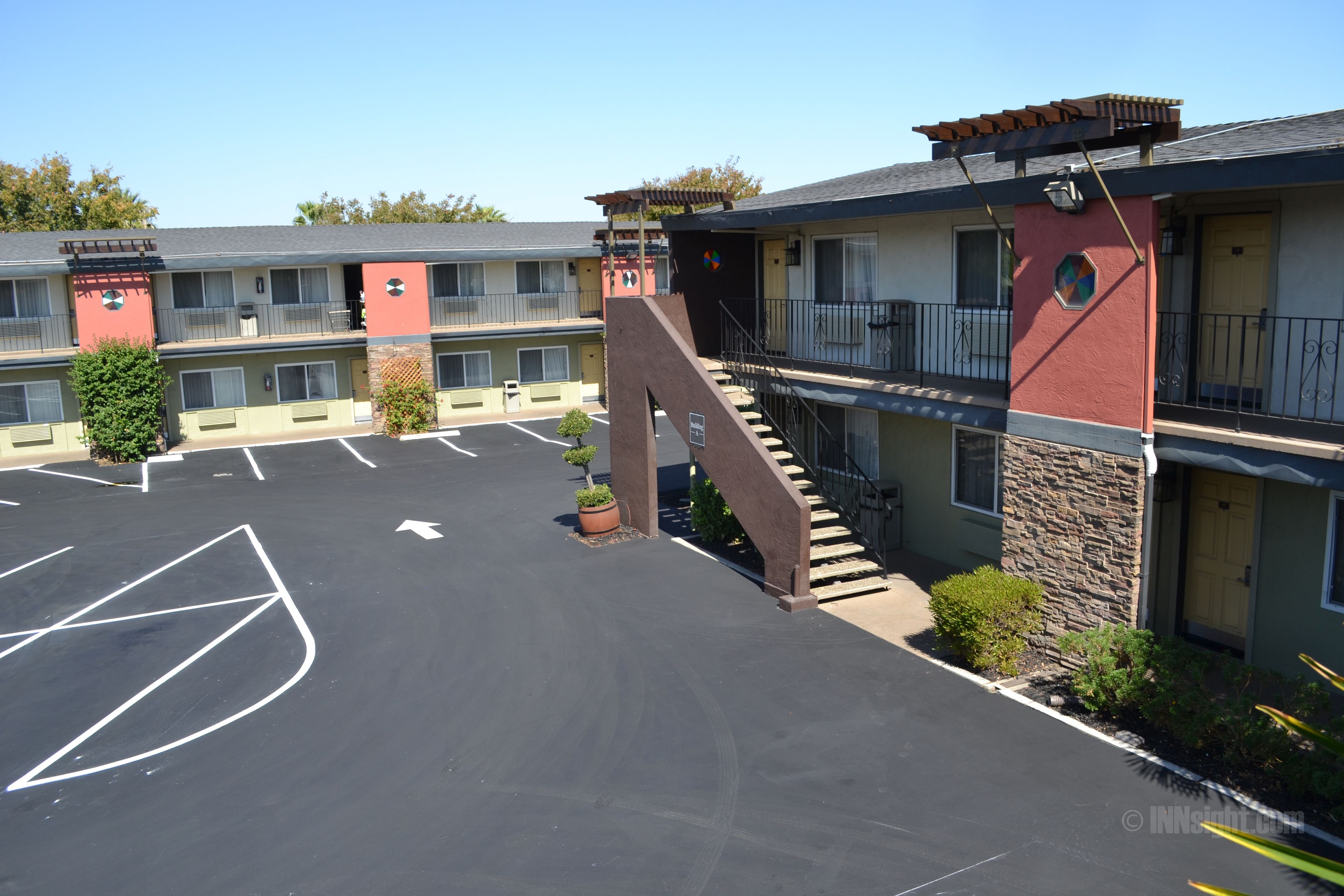 A motel with a parking lot, a staircase leading to the second floor, and a small garden area.