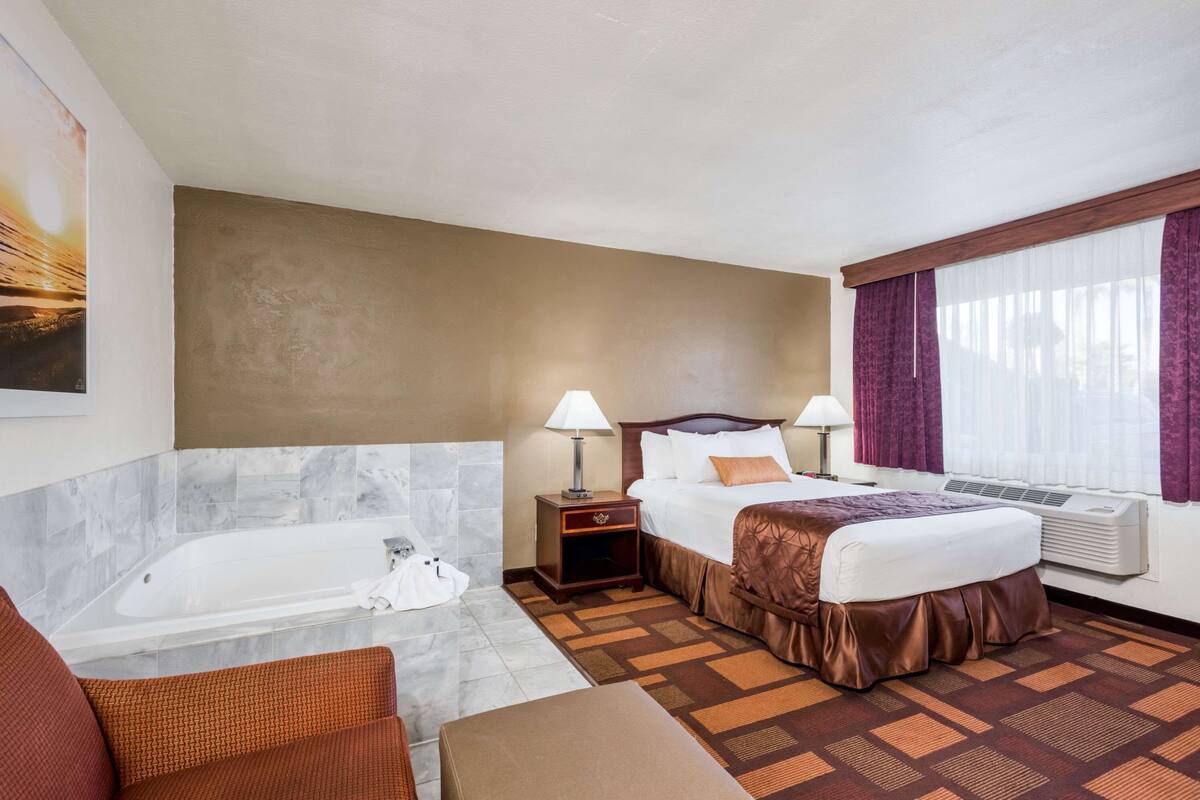 A hotel room with a large bed, a separate sofa, a bathtub, and a window with curtains.