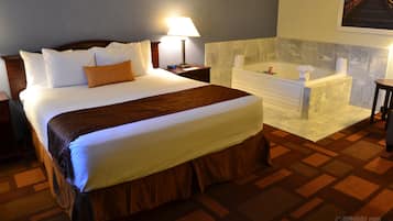 Habitación de hotel con una cama grande, un baño con bañera y una mesita de noche con lámpara.