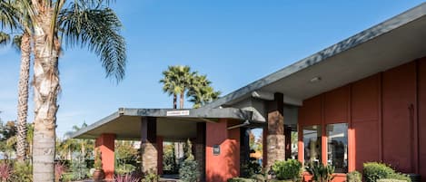 A modern building with a covered entrance, palm trees, and well-maintained landscaping.