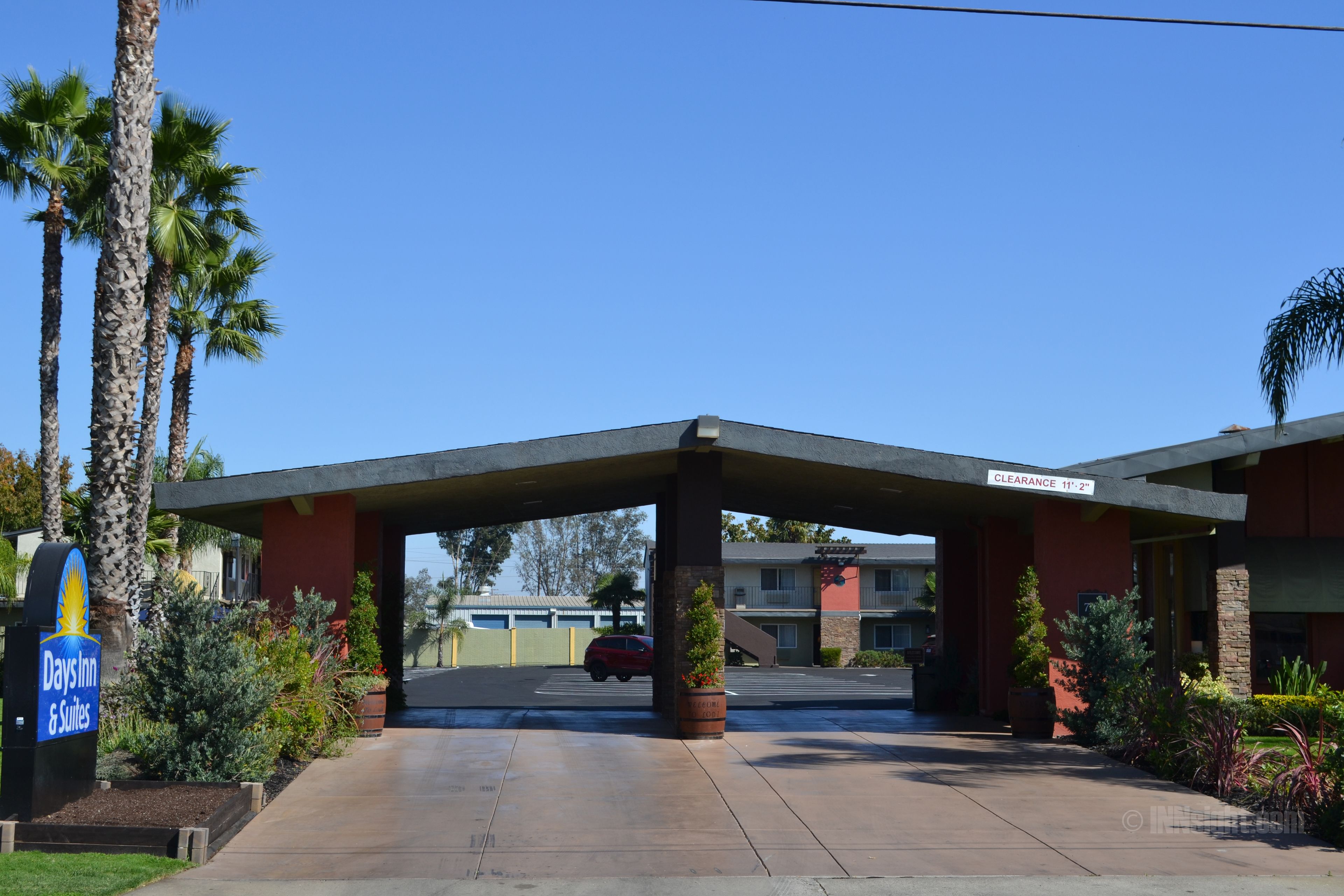 A Days Inn & Suites with a covered parking area, palm trees, and a clear blue sky.