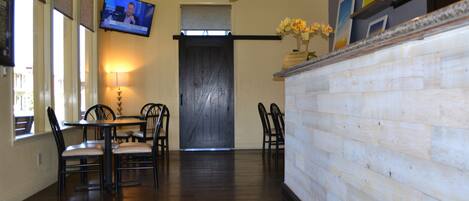 A hotel lobby with a dining area, a TV mounted on the wall, a ceiling fan, and a wooden reception desk.