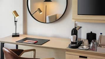 A hotel room with a desk, chair, coffee machine, and a flat-screen TV.