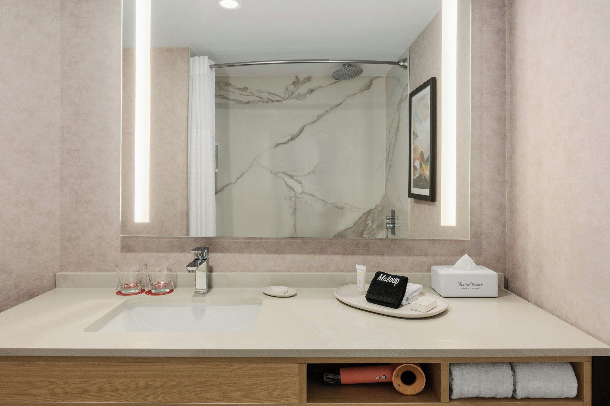 Un baño con lavamanos de mármol, un espejo, una toalla y un artículo de maquillaje.