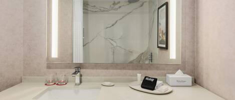 Un baño con lavamanos de mármol, un espejo, una toalla y un artículo de maquillaje.